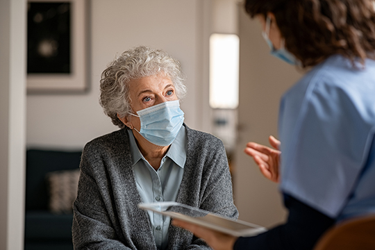 Photo of an older adult listening to a healthcare provider. Both are wearing masks.