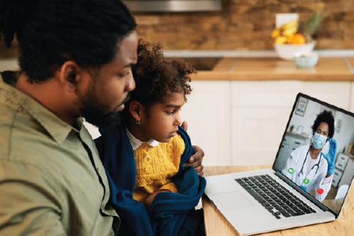 A parent and child sitting in their kitchen meet with a primary care provider using a laptop.