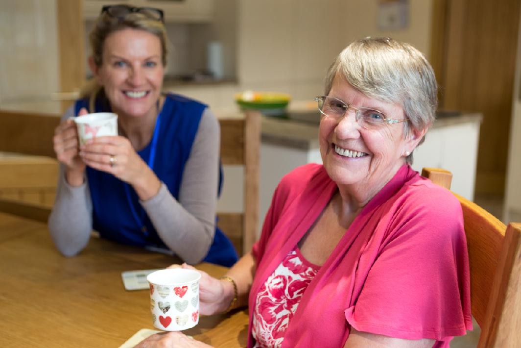 Healthcare worker and patient smiling together drinking from a mug